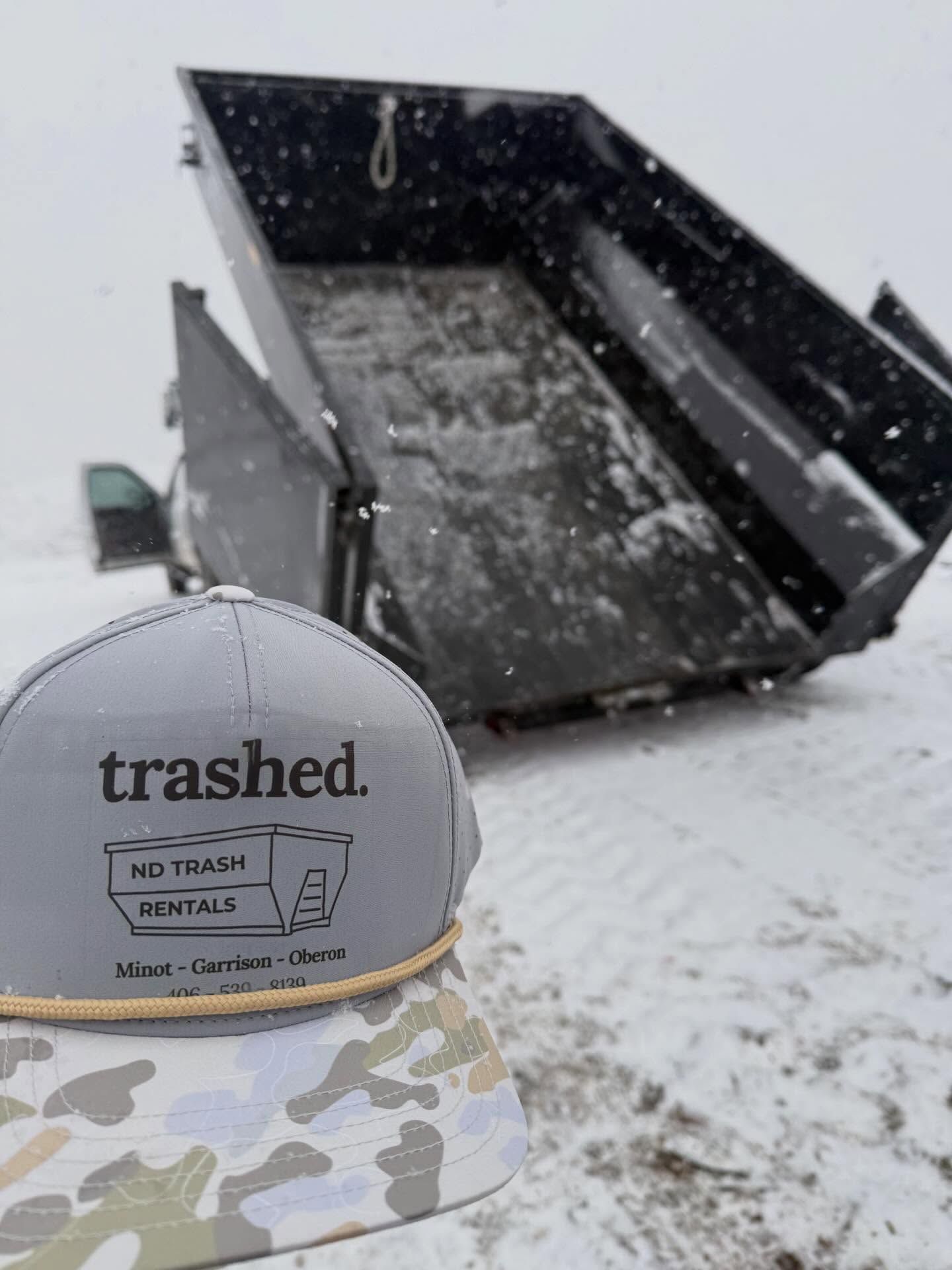 Snowy construction dumpster with a camo cap reading “trashed.”