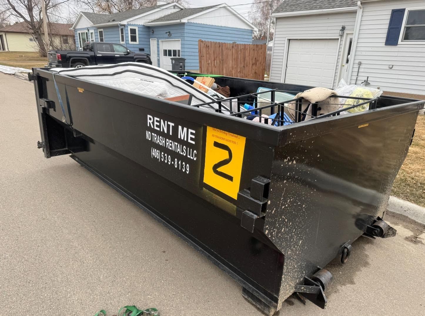 Black construction dumpster on a residential street, labeled 