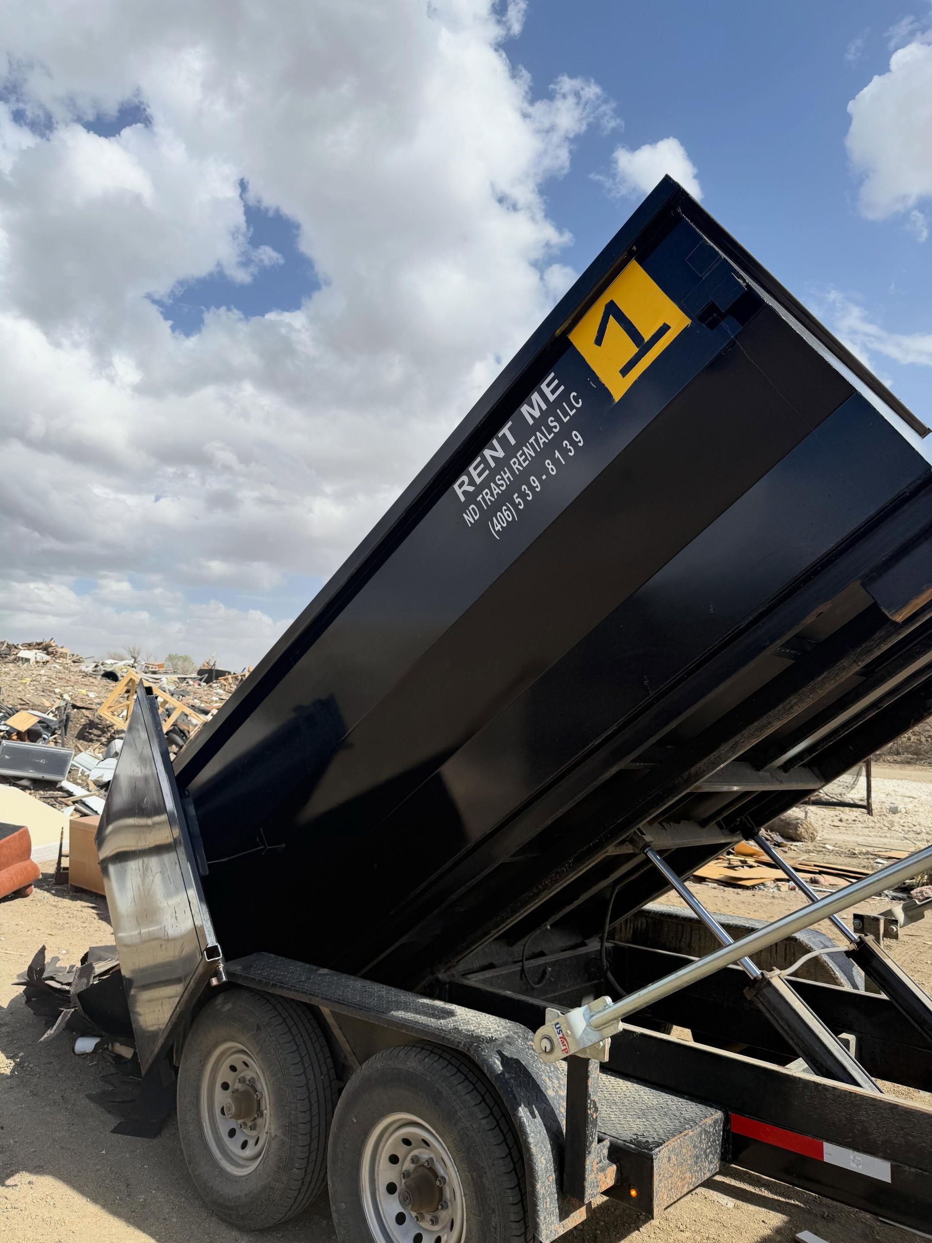 Black dump trailer tipped up at a construction site under a cloudy sky