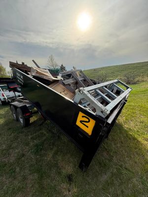 Damaged black trailer tipped on its side in a grassy field under a bright sun.