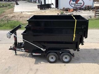 Black dump trailer with two axles and a yellow strap parked on concrete near a building