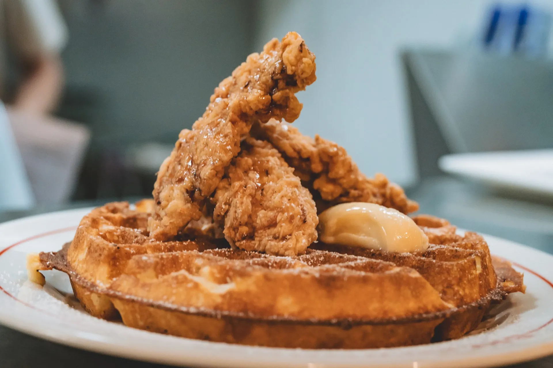 Chicken and waffles with powdered sugar and butter on a white plate.