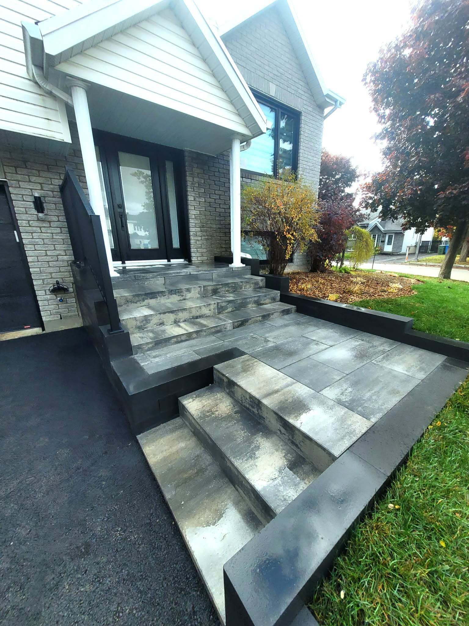 Un escalier et une rampe mènent à l'entrée de la maison, revêtue de pierre grise et bordée de noir.