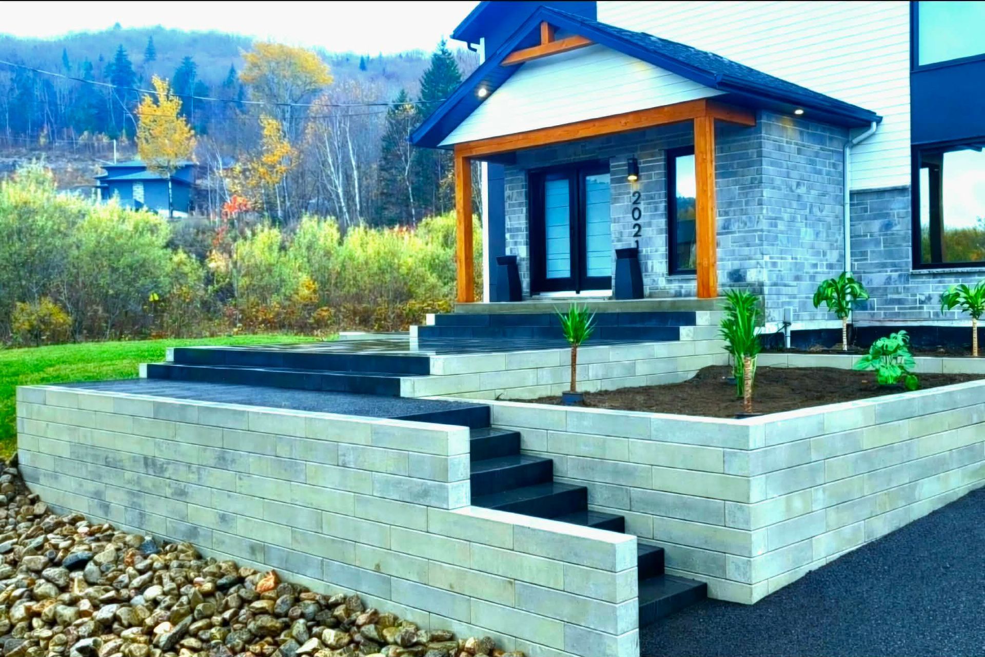 Maison moderne avec marches en pierre, parterres de jardin surélevés et aménagement paysager rocailleux dans un cadre rural