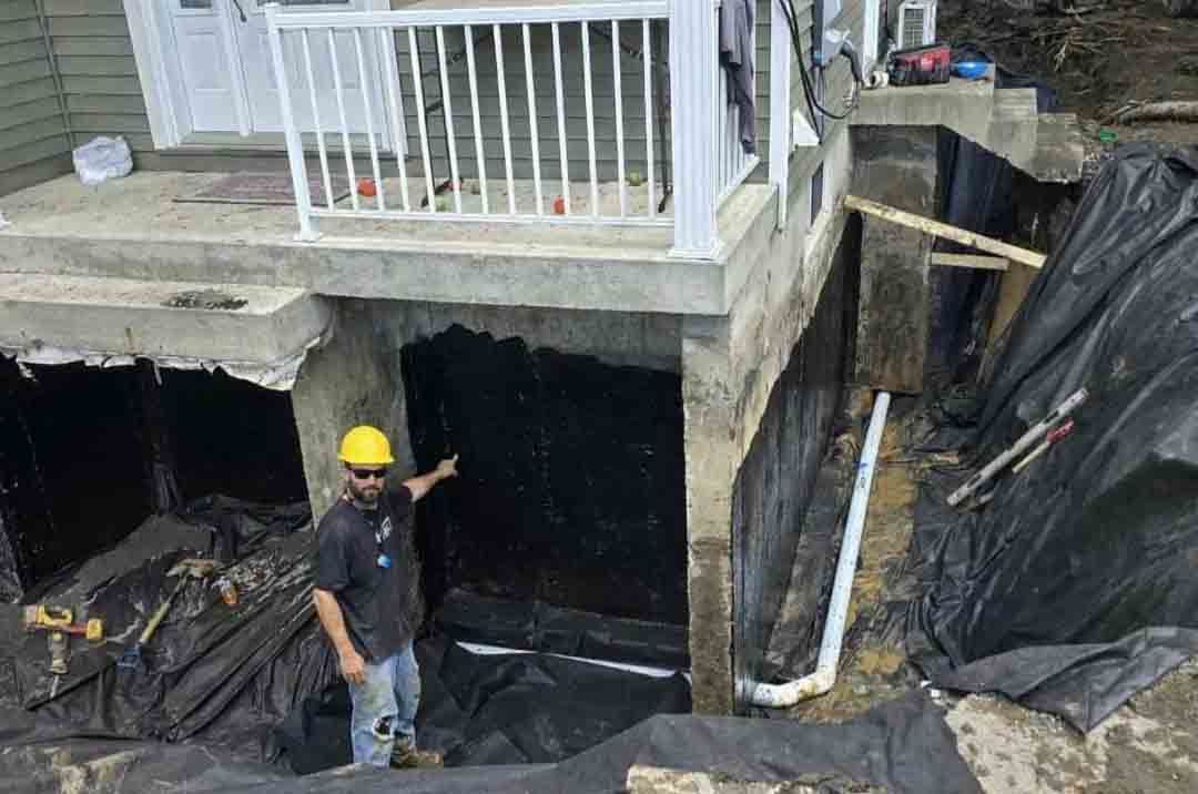 Une tranchée a été creusée à côté d'une maison et tapissée de tissu. Des tuyaux blancs ont été installés pour le système de drainage.