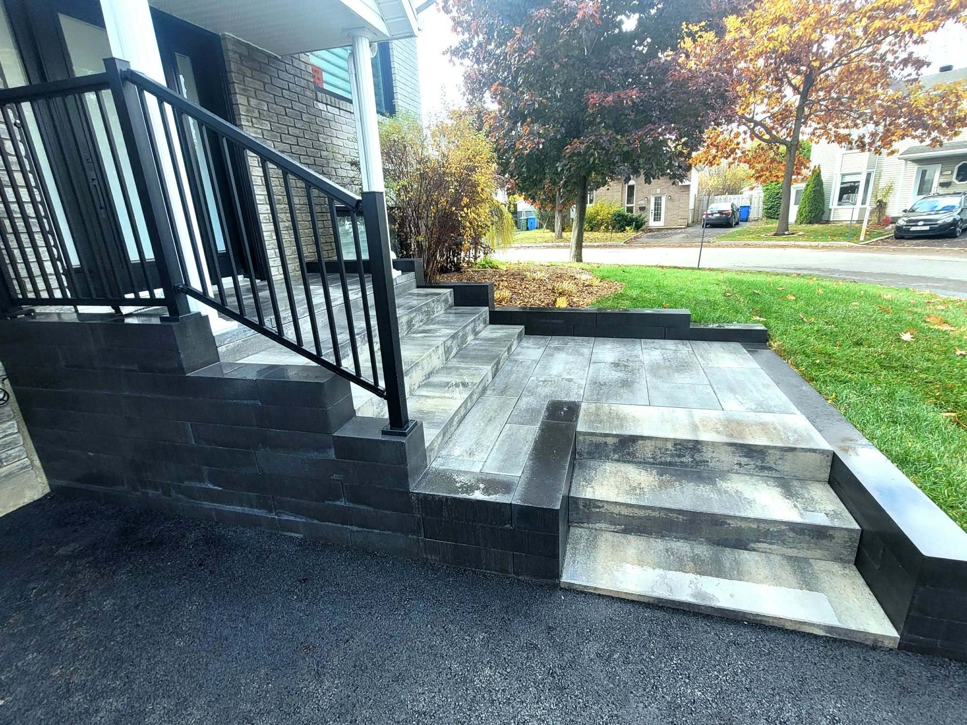 Escalier et rampe d'accès en béton à côté de la maison, avec rambarde noire et cour gazonnée