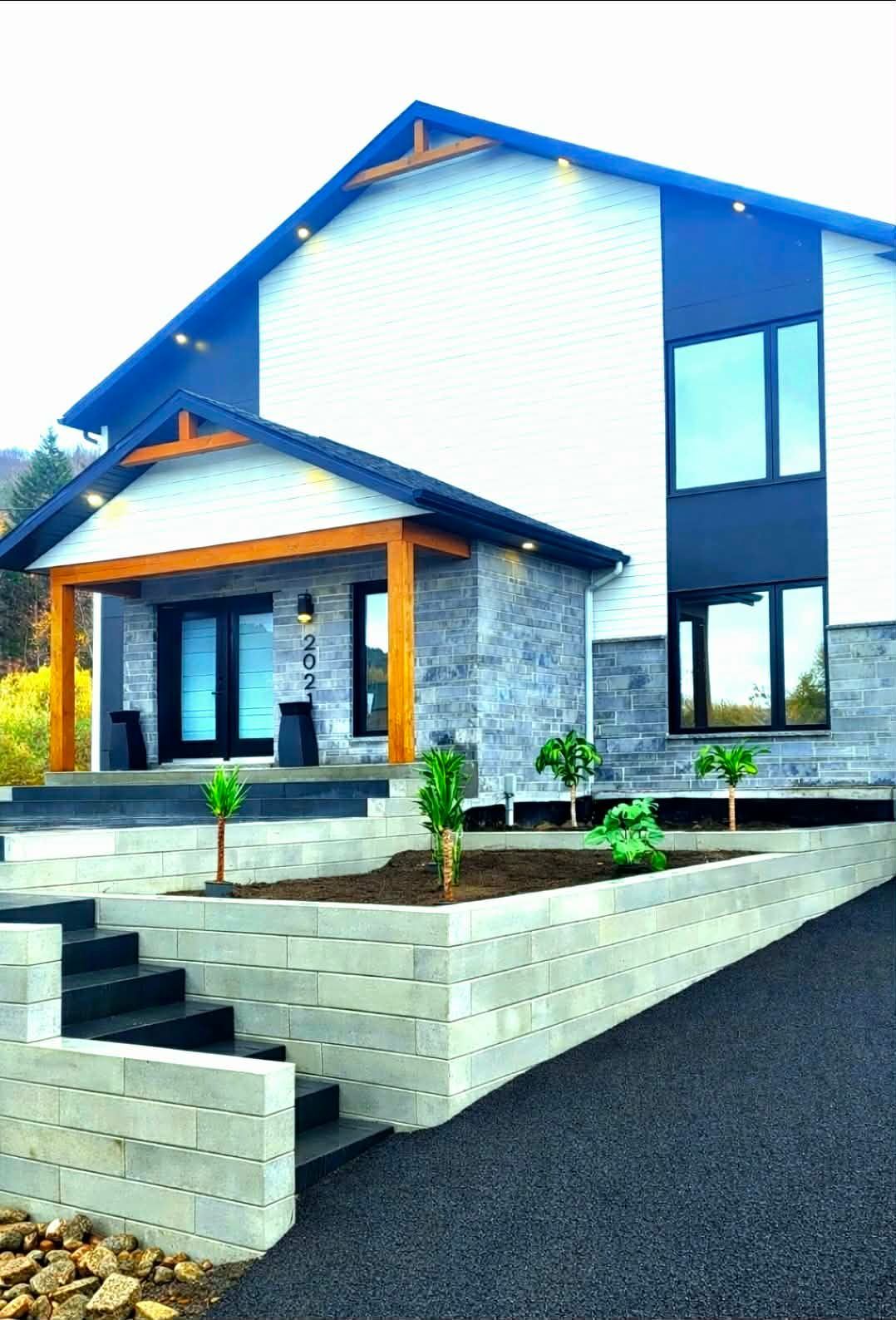 Maison moderne à deux étages avec toit bleu, façade en pierre et perron paysagé.