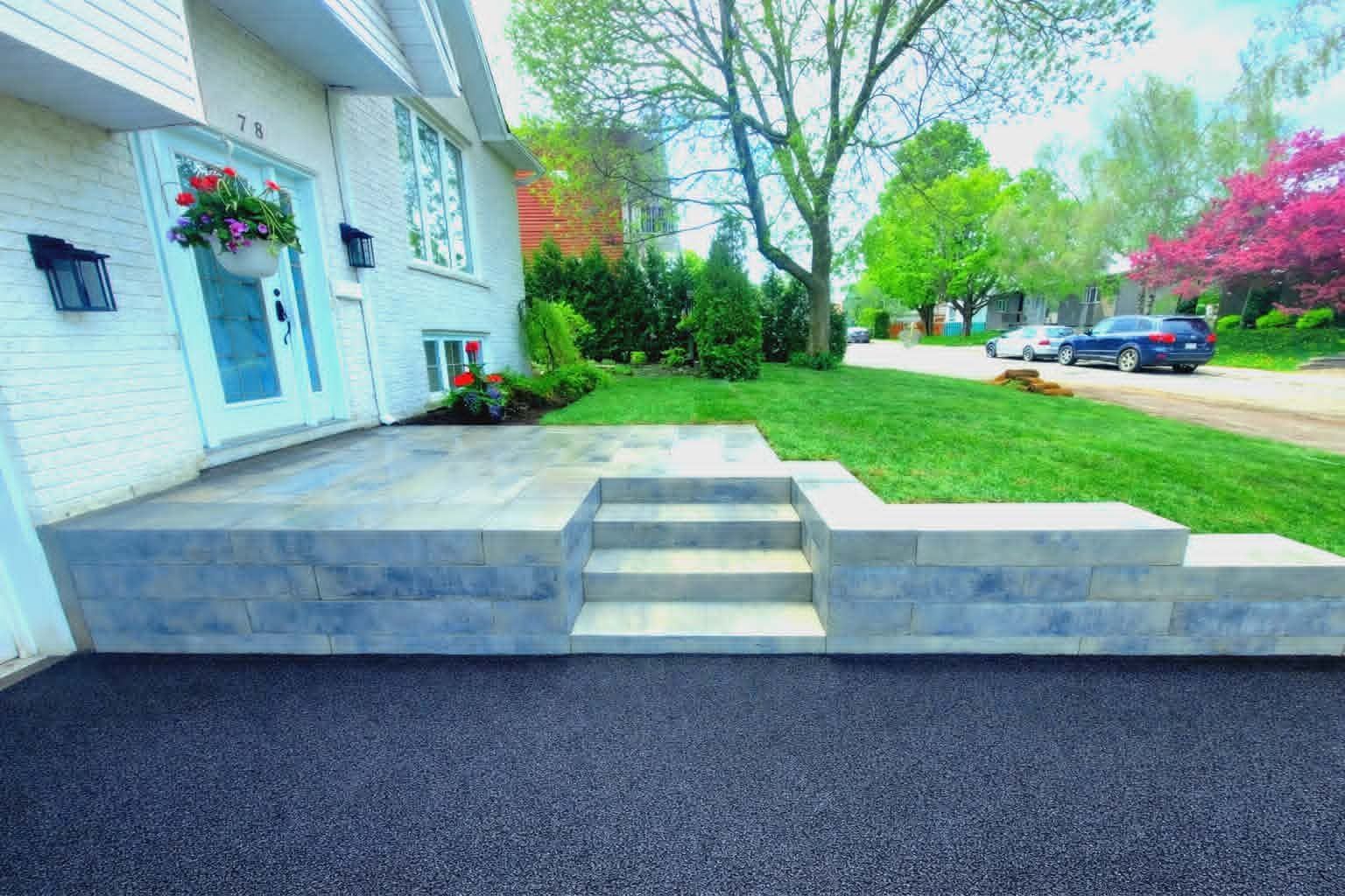 Marches et rampe d'accès à une maison blanche à porte bleue, à côté d'une pelouse verte et d'une rue.