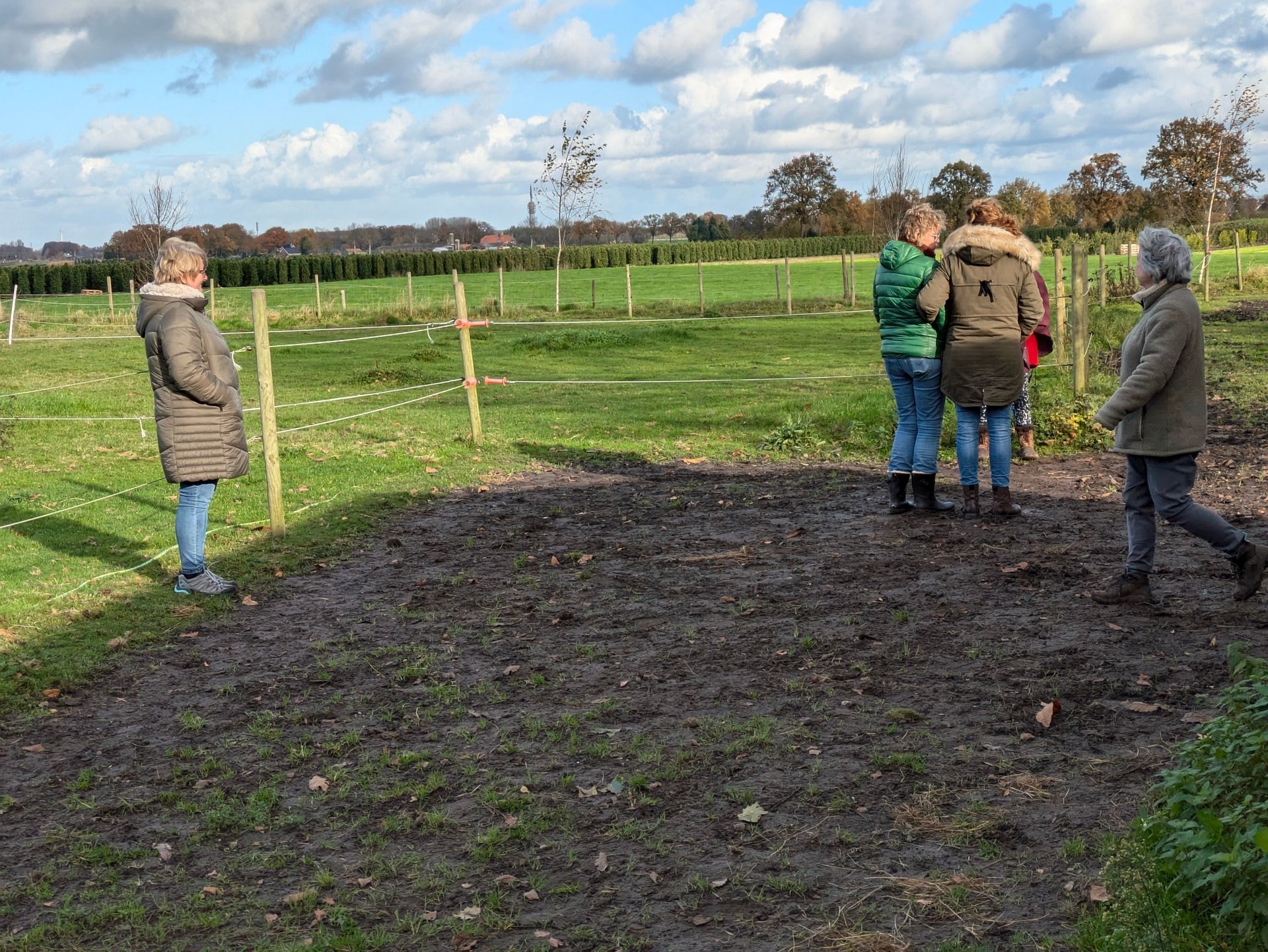 Mensen staan op een bewolkte dag bij een modderig stuk grond in een veld.