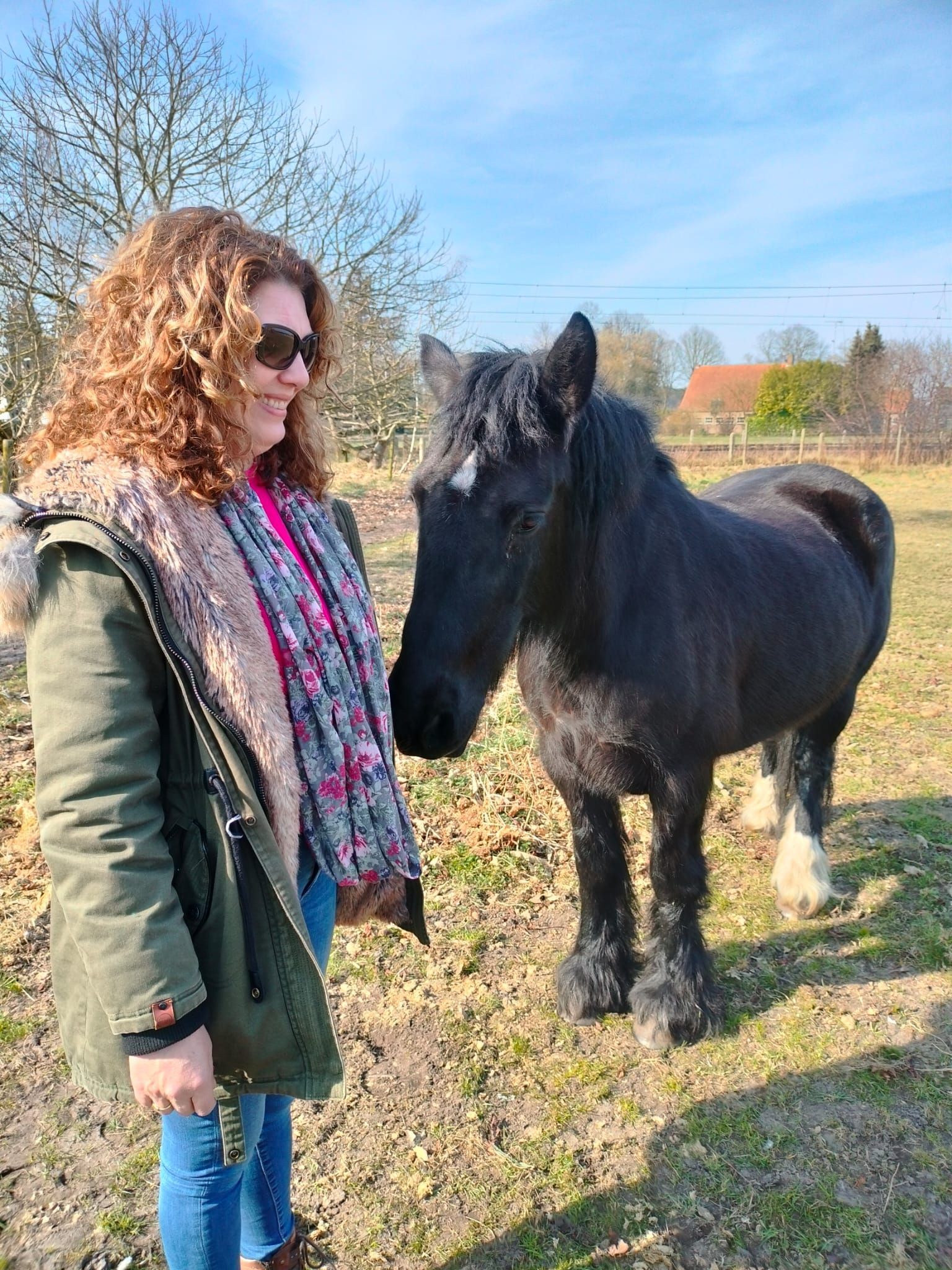 Vrouw met zonnebril staat met een paard buiten in de wei.