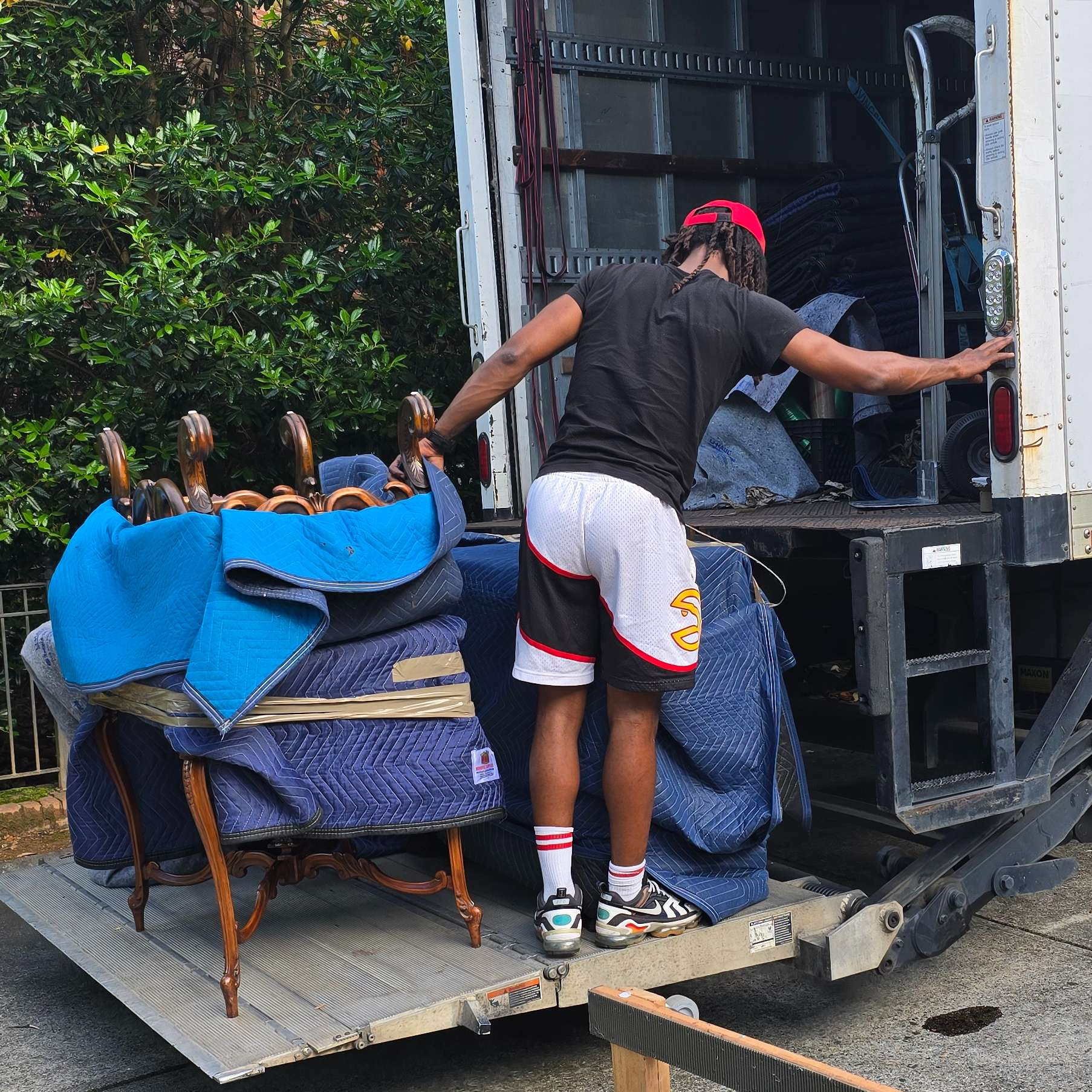 A person loads furniture onto a truck ramp. The person wears shorts, a shirt, and socks.