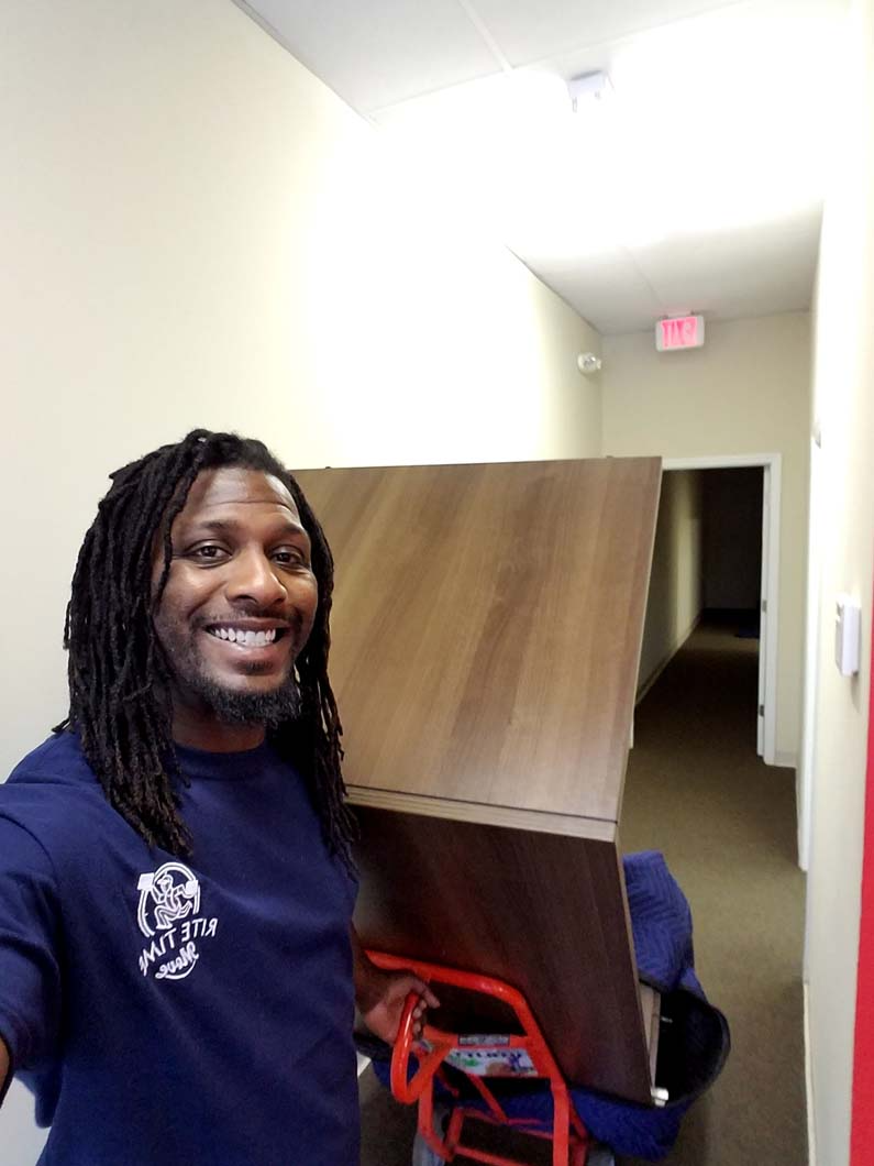 Man smiling, moving large wood panel on a dolly down a hallway.