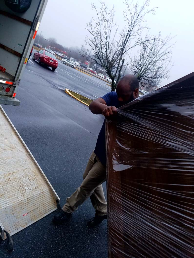 Man moving a large wrapped item from a truck in wet conditions.