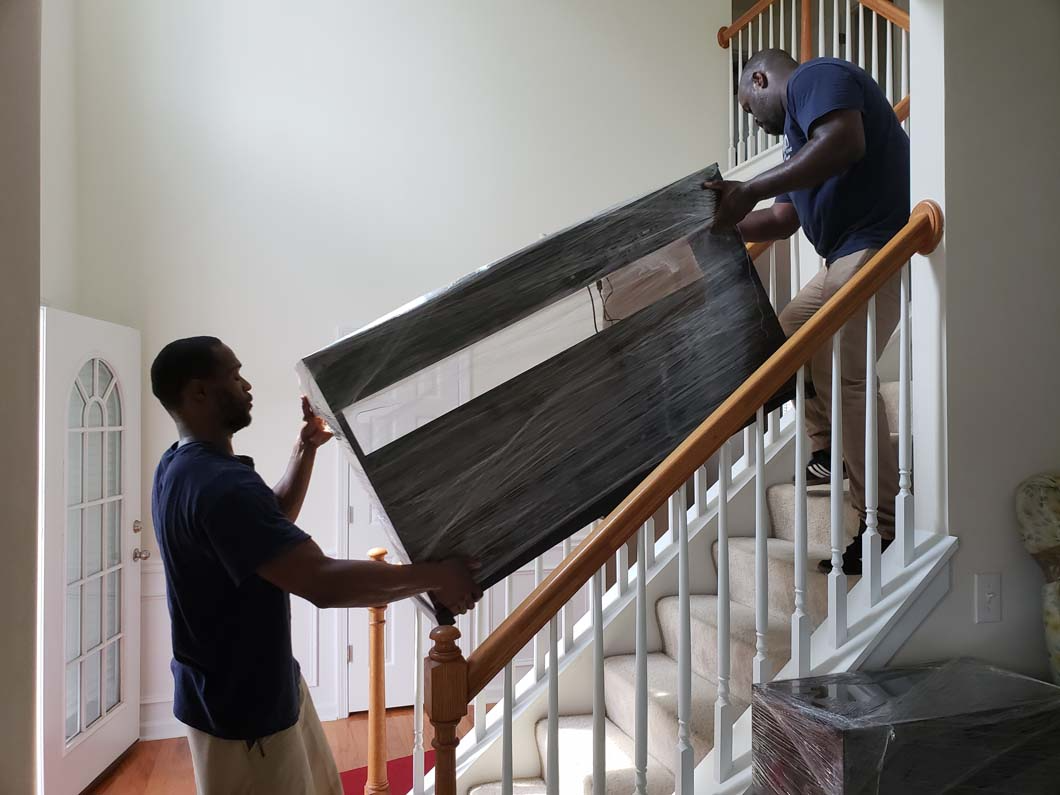 Two people moving a wrapped rectangular item up a staircase.