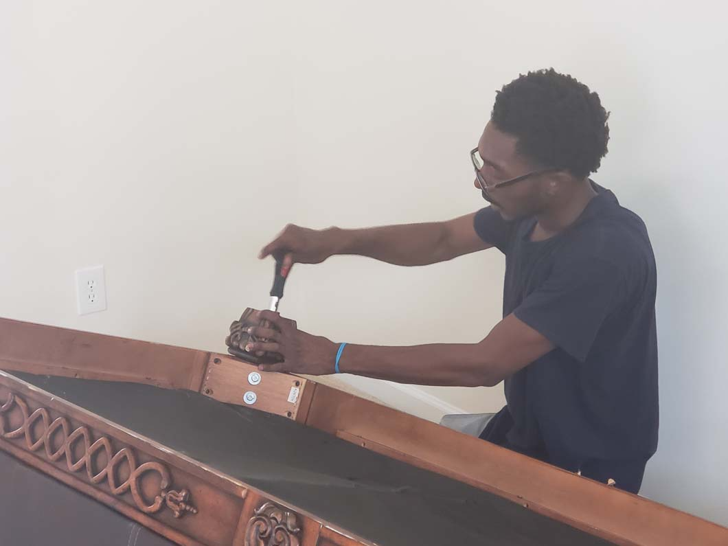 Person using a screwdriver to assemble a brown wooden structure against a white wall.