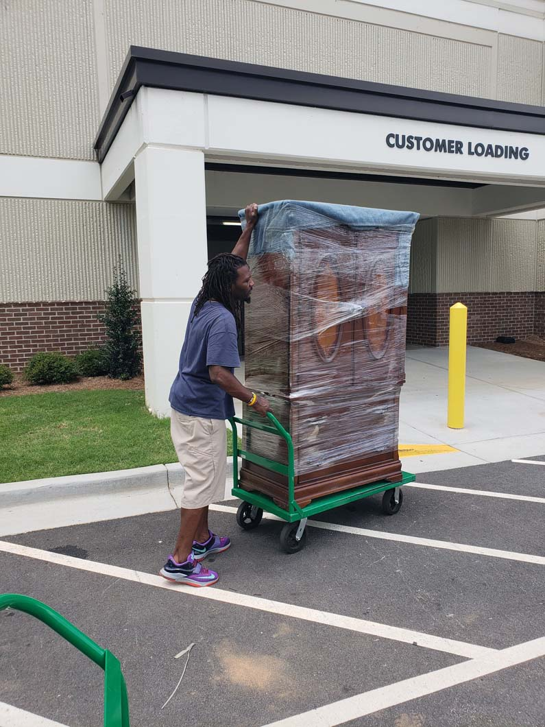 Person pushing a tall, wrapped object on a green cart in front of a 