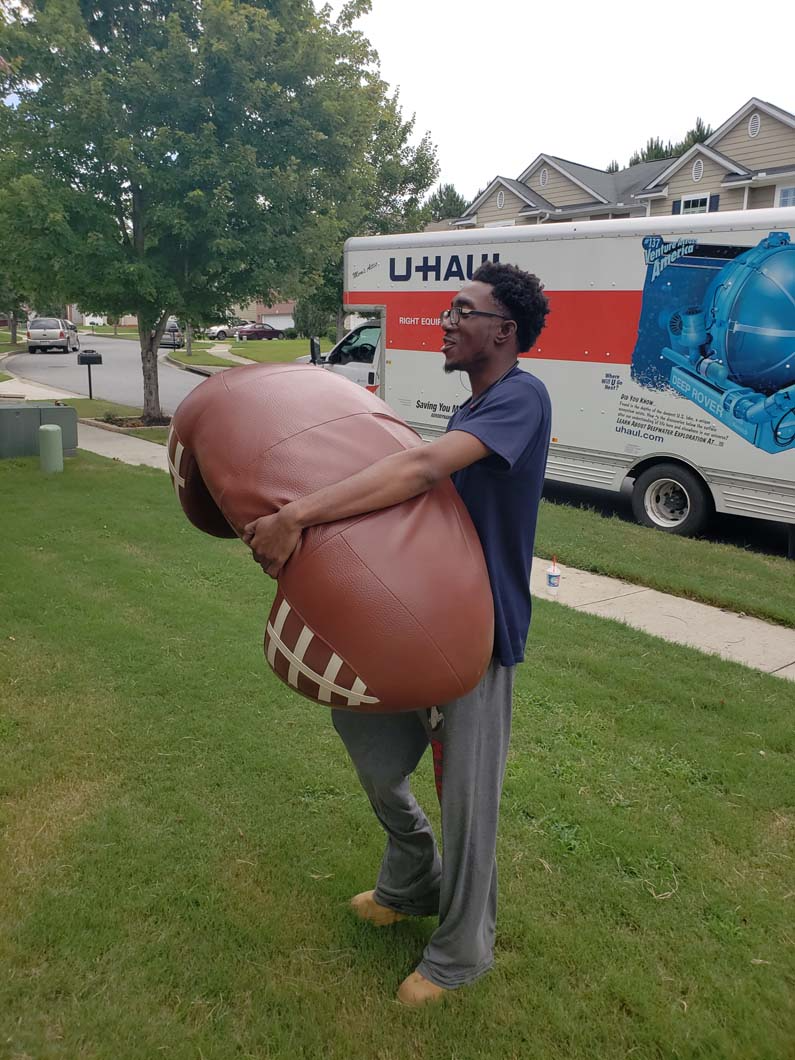 Person carrying a large inflatable football in front of a U-Haul truck.