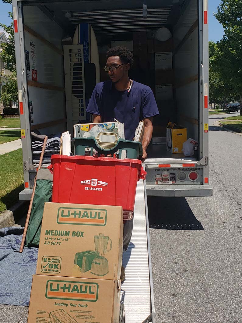 Man loading boxes and bins from U-Haul truck. Sunny outdoor setting.