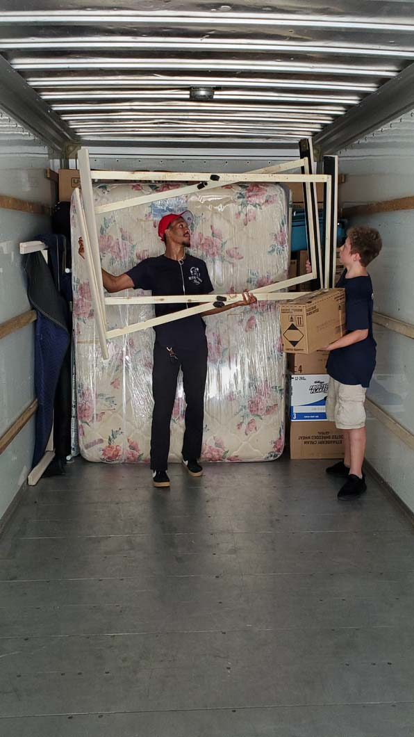 Two people loading a moving truck with a mattress, frame, and boxes.