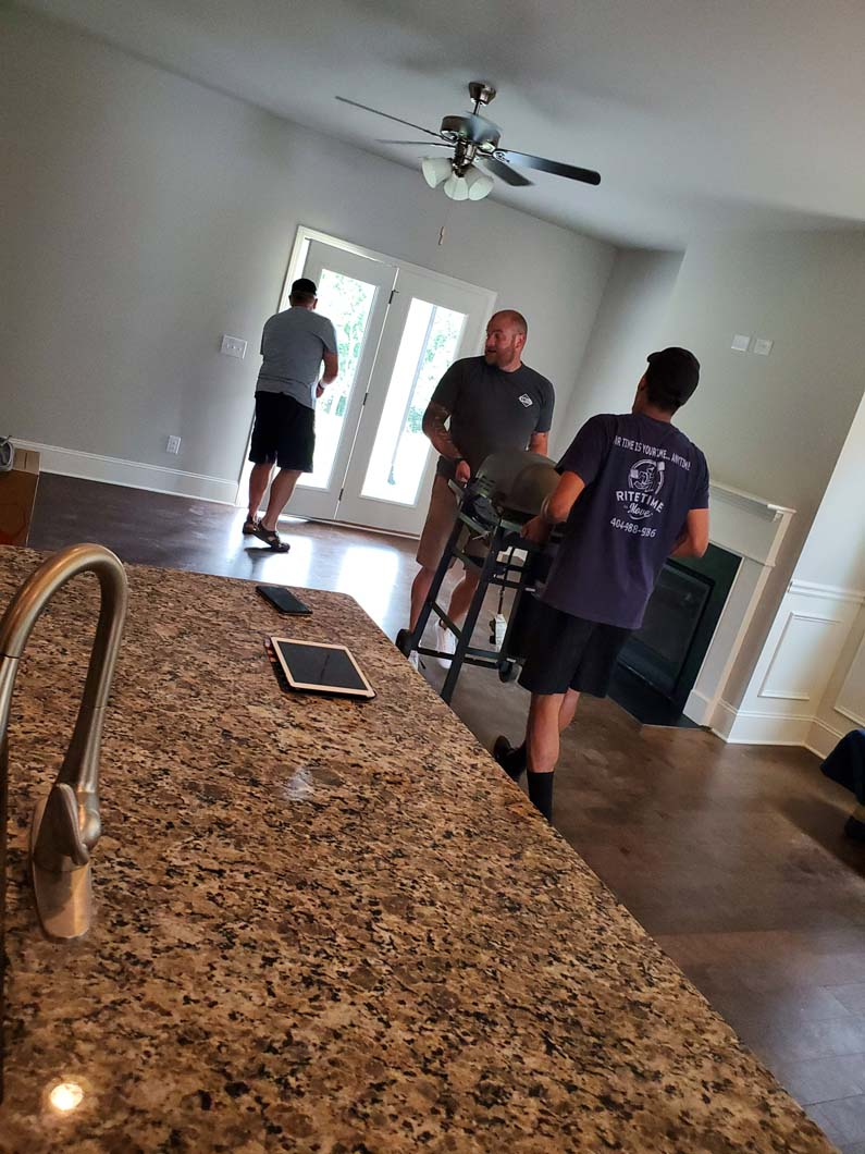 Three people moving furniture through French doors in a light-filled living room.