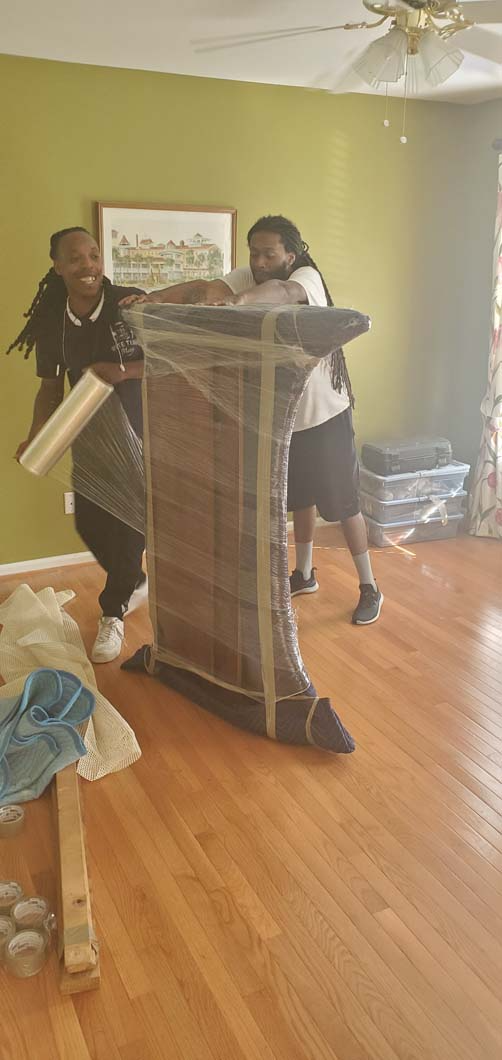 Two people wrapping a table in plastic in a room with hardwood floors.