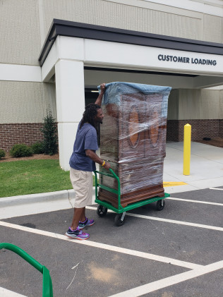 Person pushing a wrapped, bulky load on a cart toward a