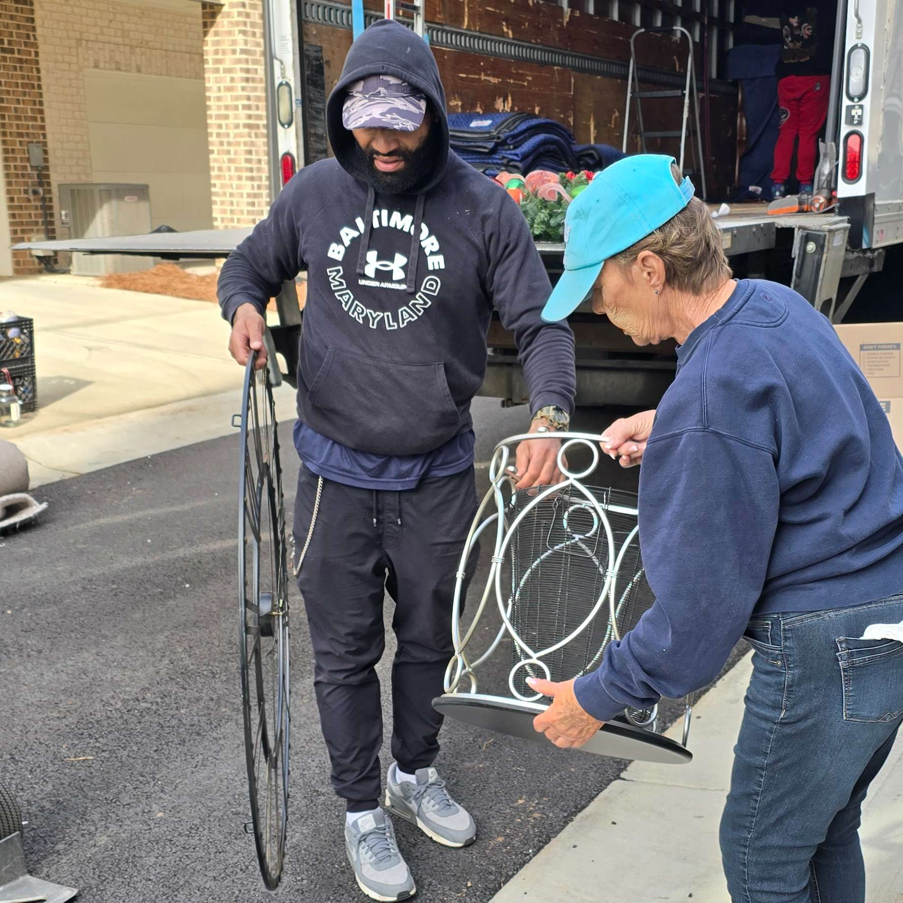 Two people unloading items from a moving truck: a bicycle wheel and decorative metal piece.