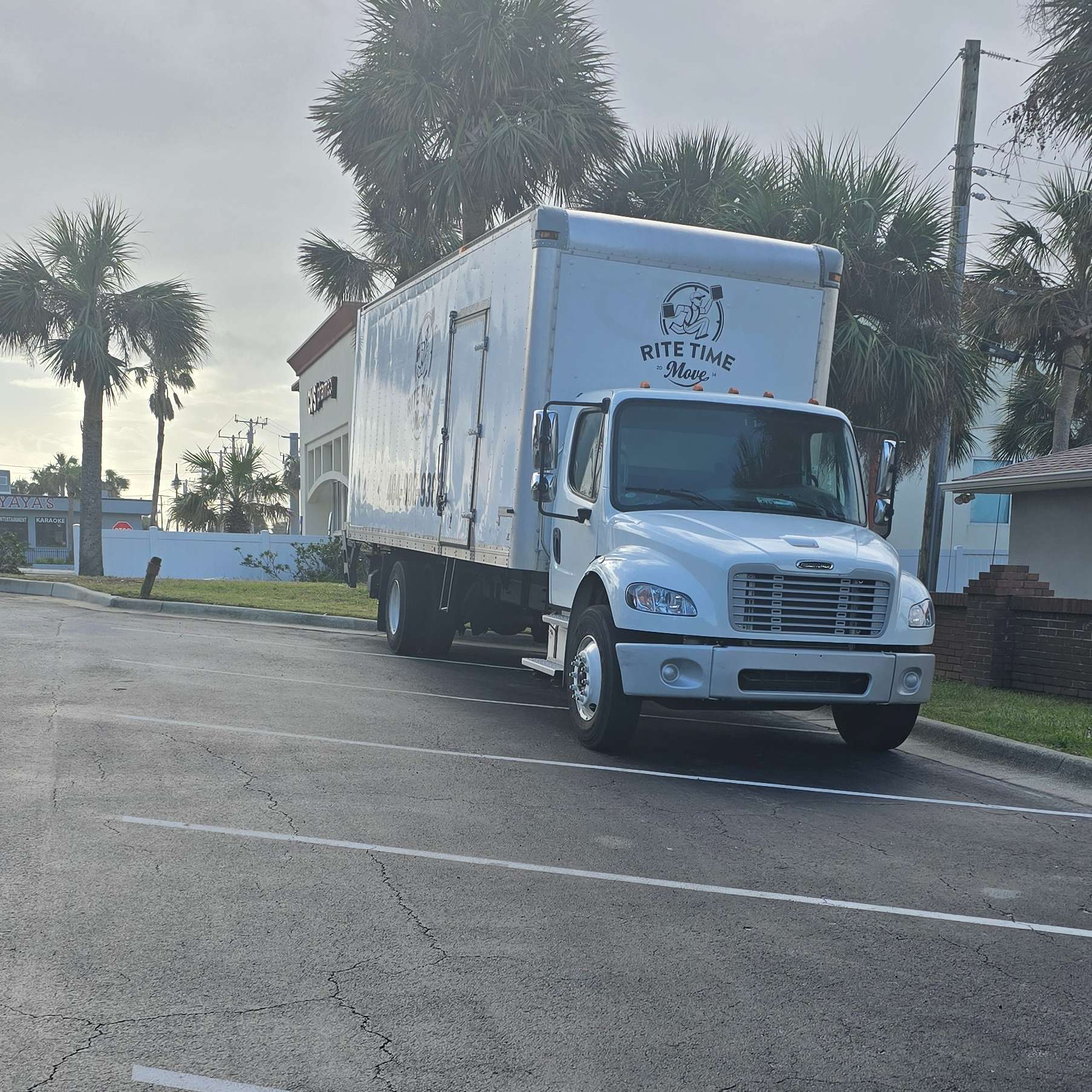 White delivery truck parked on a street near palm trees and a building.