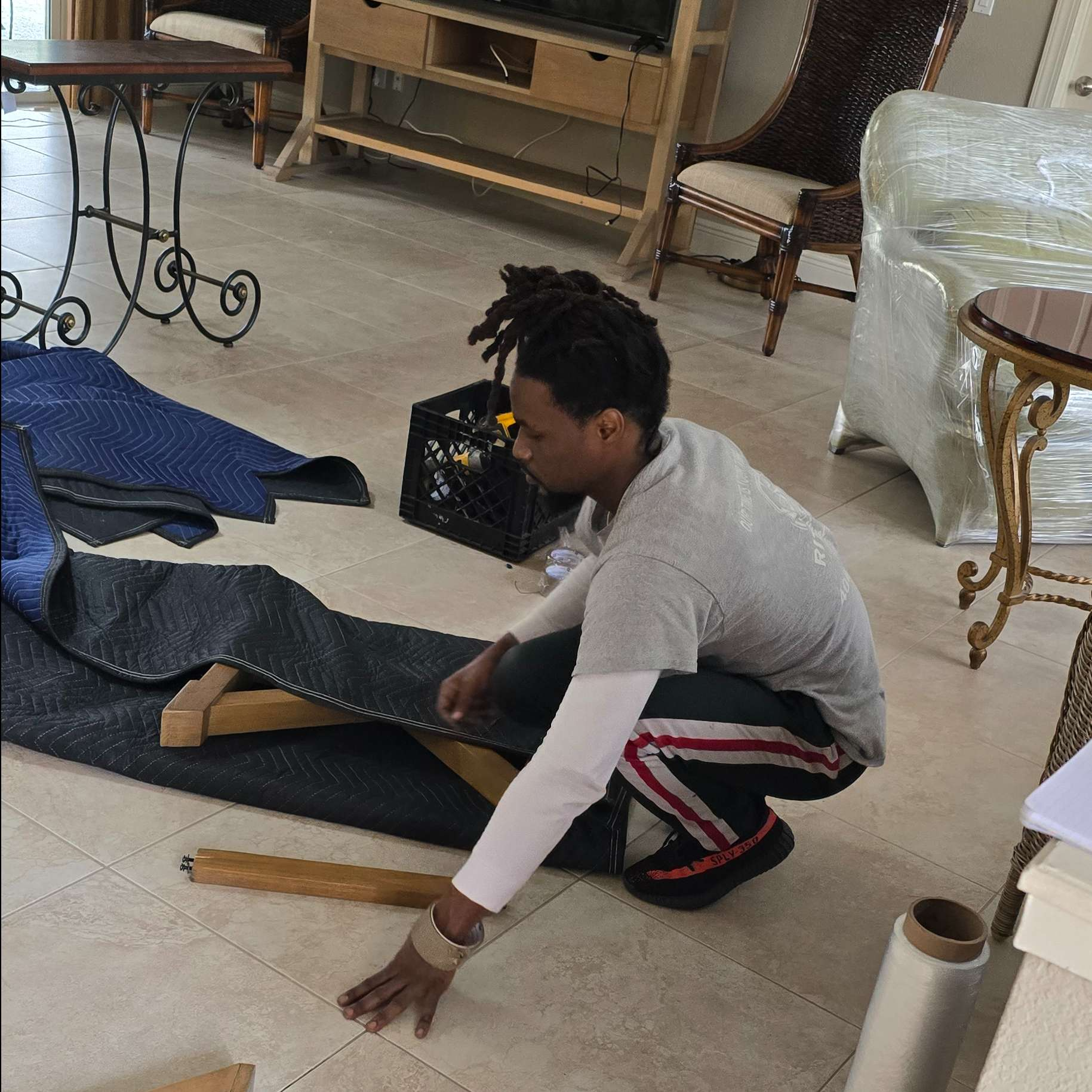 Man squatting, wrapping furniture leg with a protective blanket indoors.