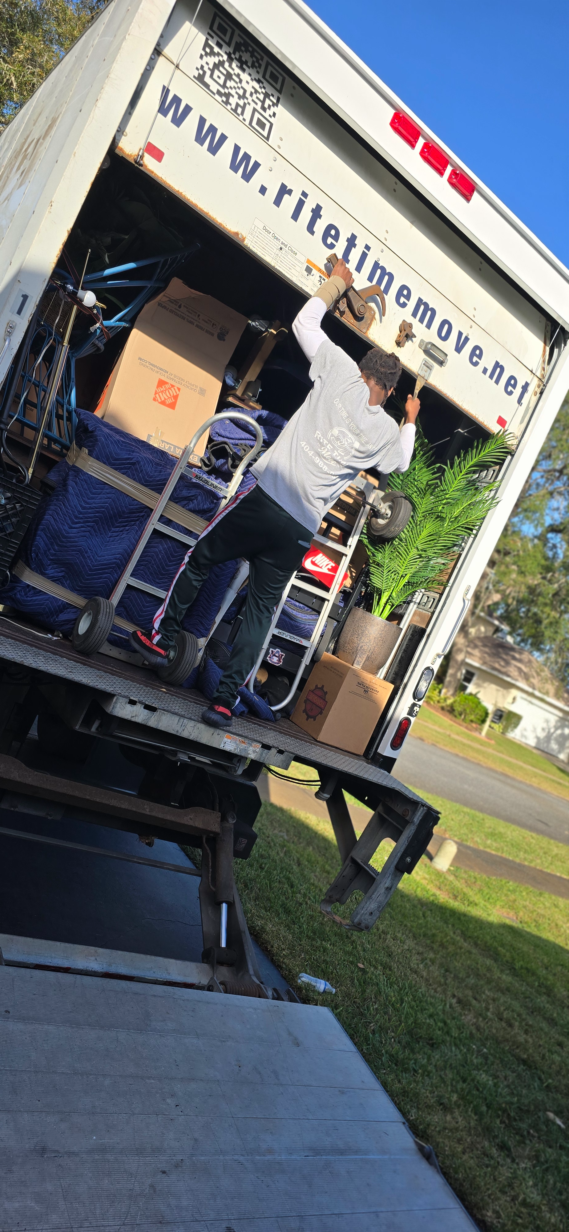 Man unloading a moving truck, holding something overhead. The truck bed is full of items.