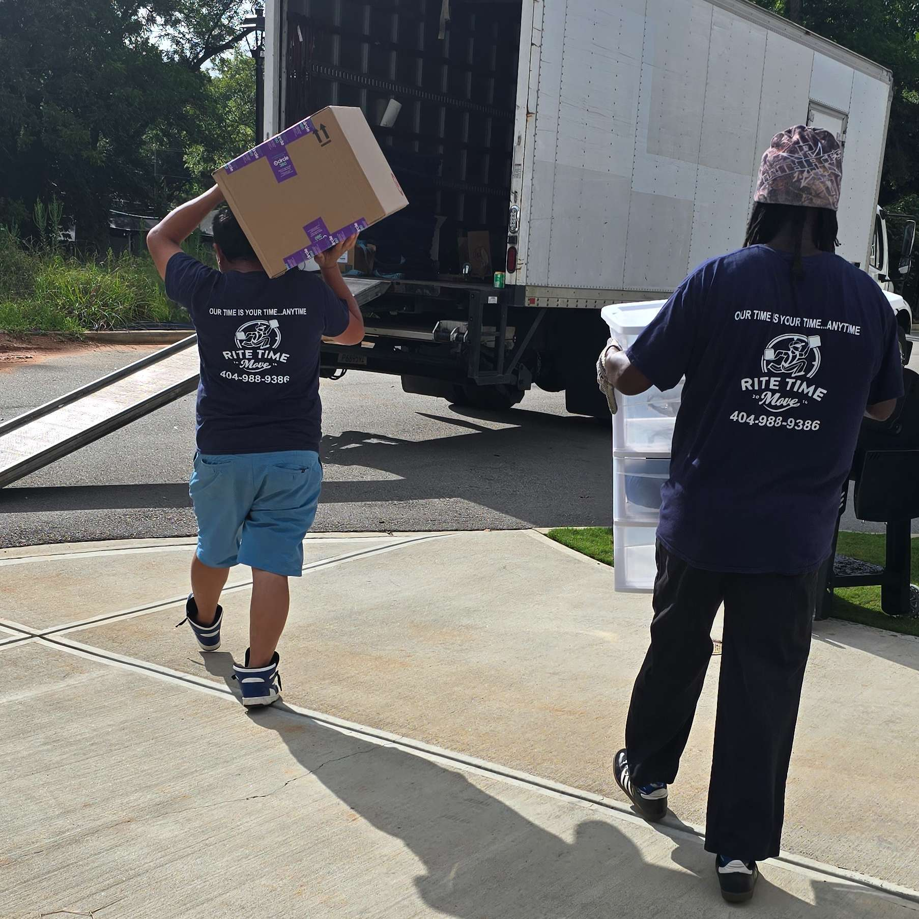 Two movers carrying boxes from a moving truck on a sunny day.