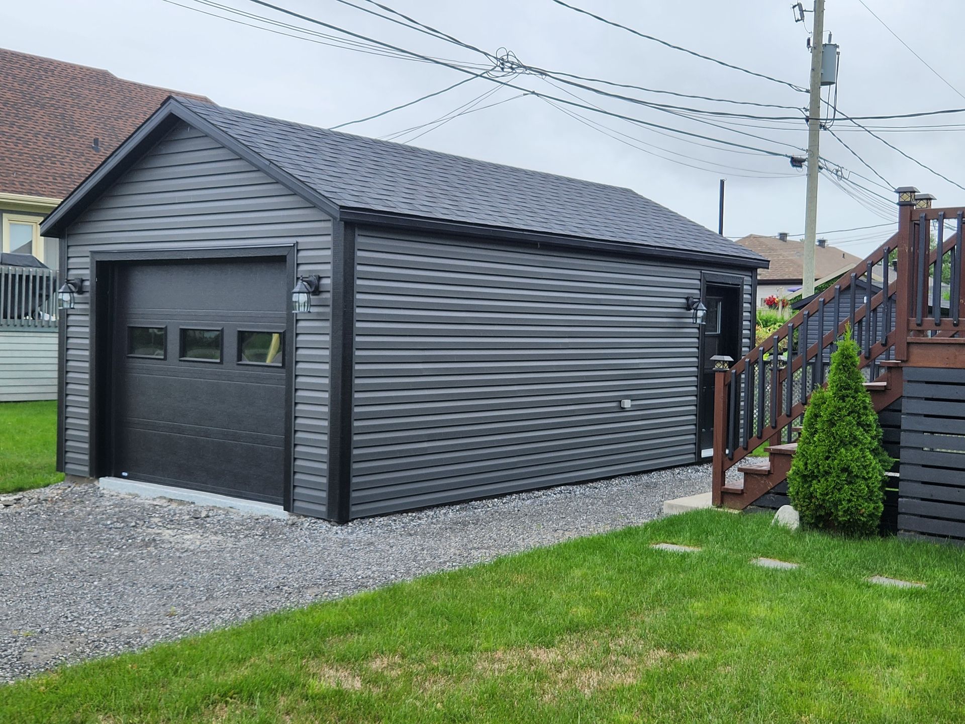 Un garage noir avec une porte noire se trouve dans l'arrière-cour d'une maison.