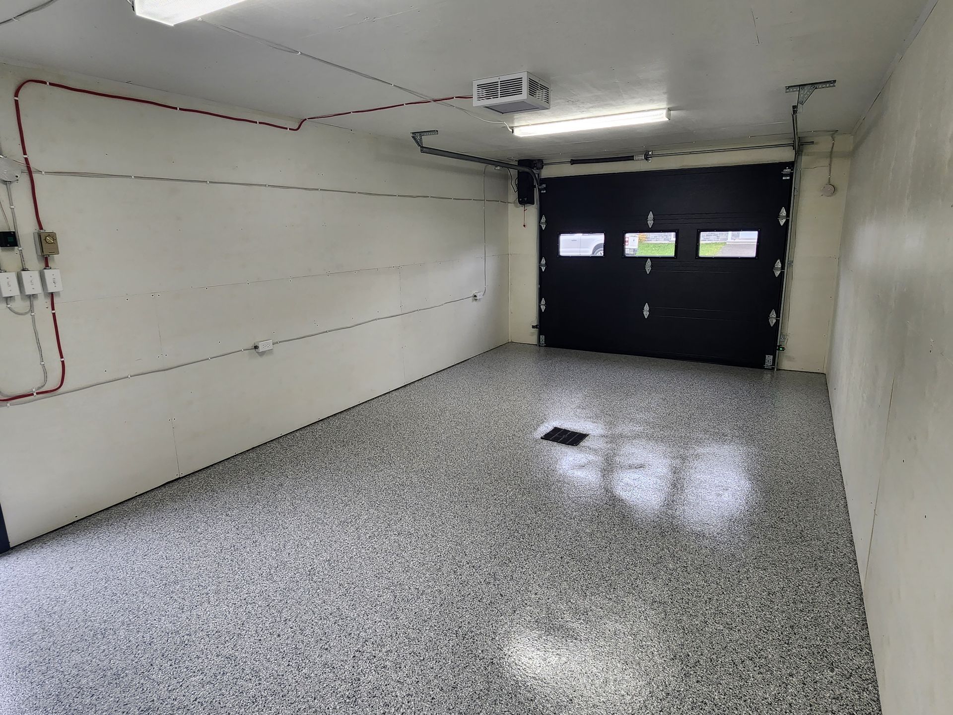 Un garage vide avec une porte de garage noire et un mur blanc.