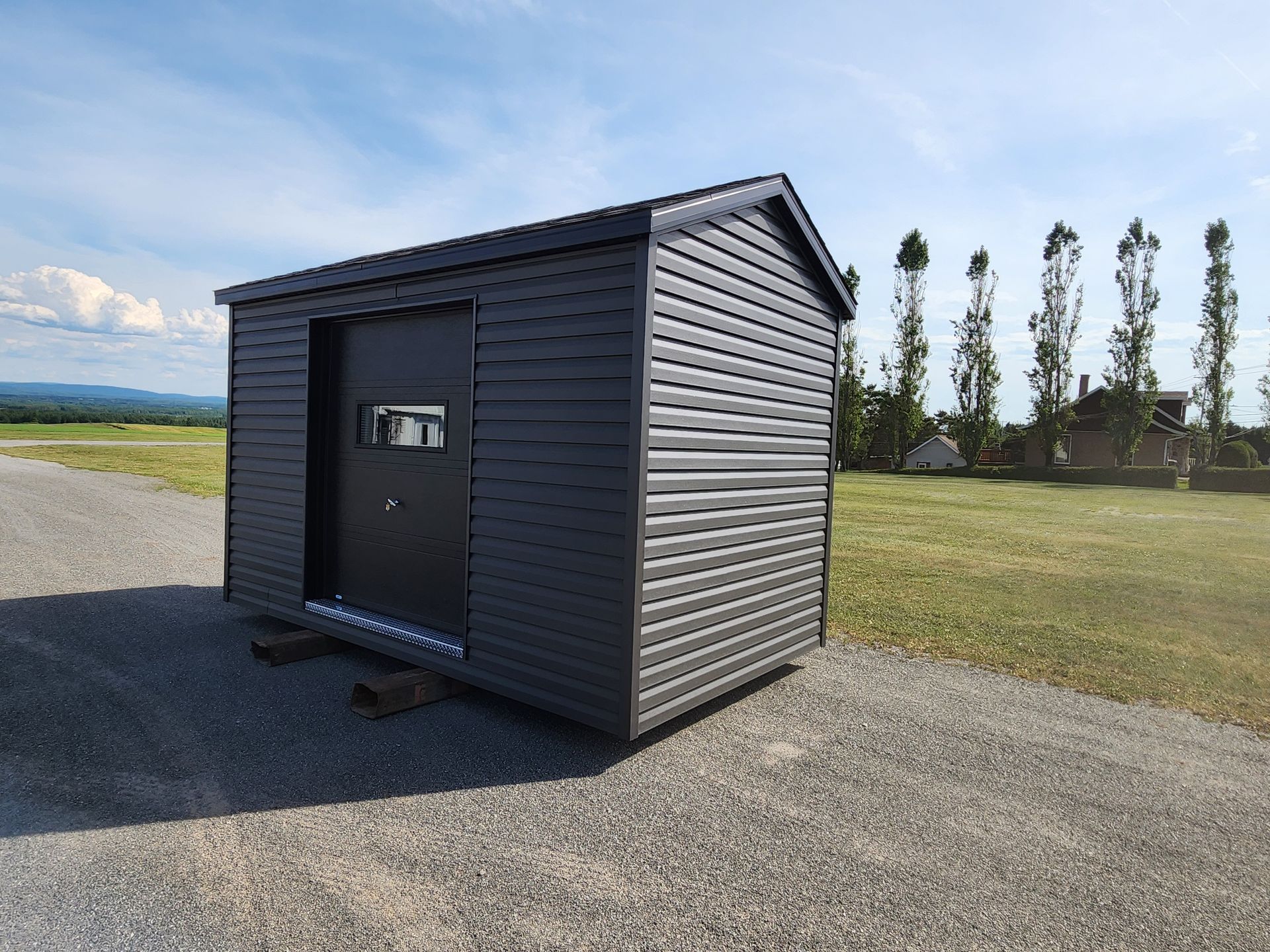 Un petit hangar noir se trouve au milieu d'un chemin de gravier.