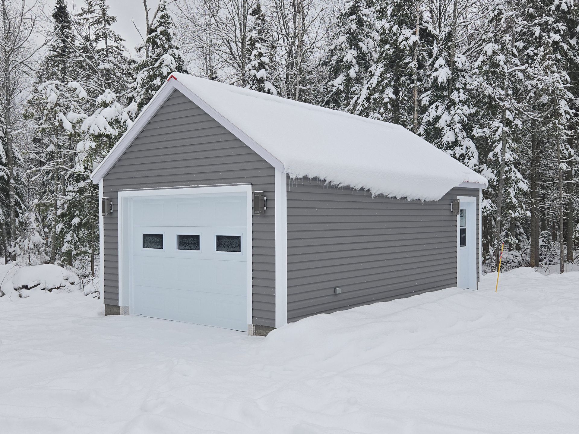 Un garage recouvert de neige avec des arbres en arrière-plan.