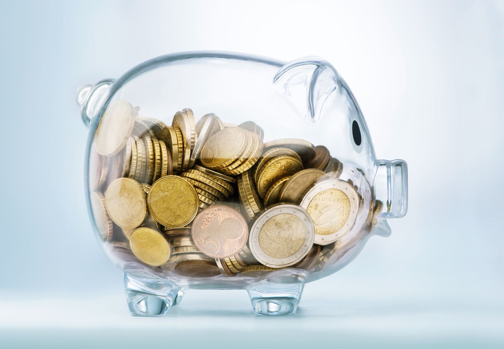 A glass piggy bank filled with coins on a table.