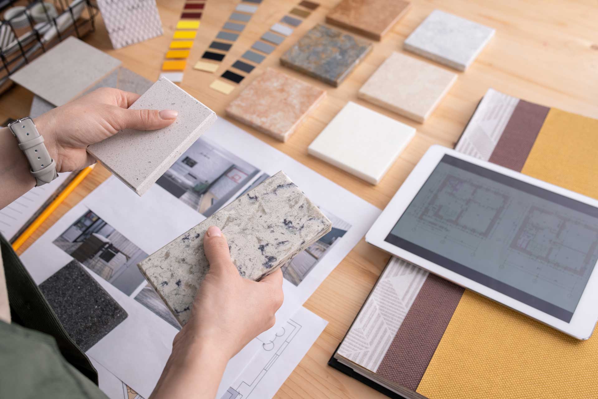 A person is sitting at a table looking at tiles and a tablet.