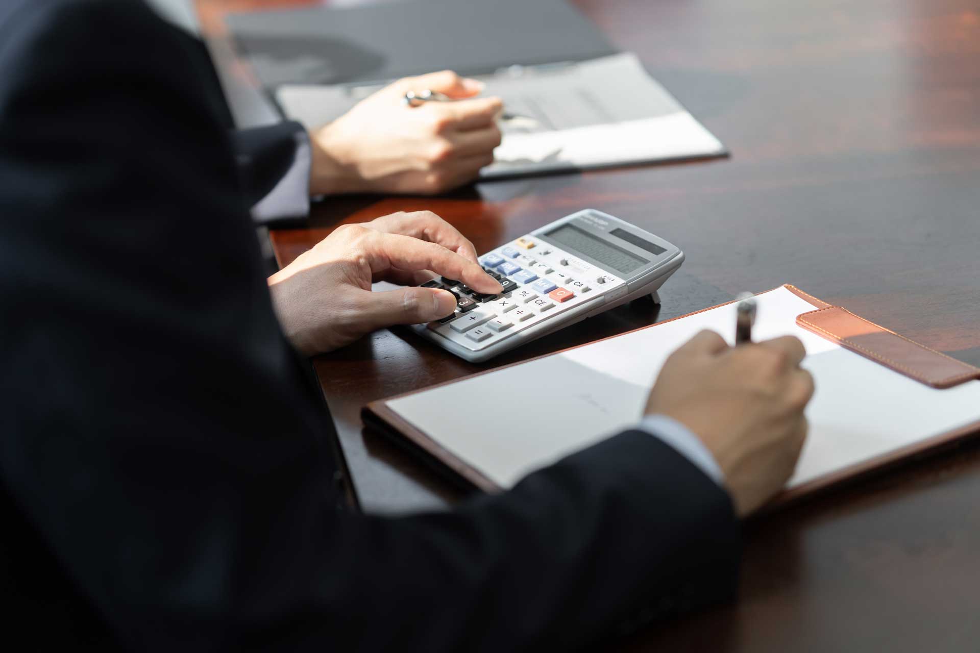 A man is sitting at a table using a calculator and writing in a notebook.