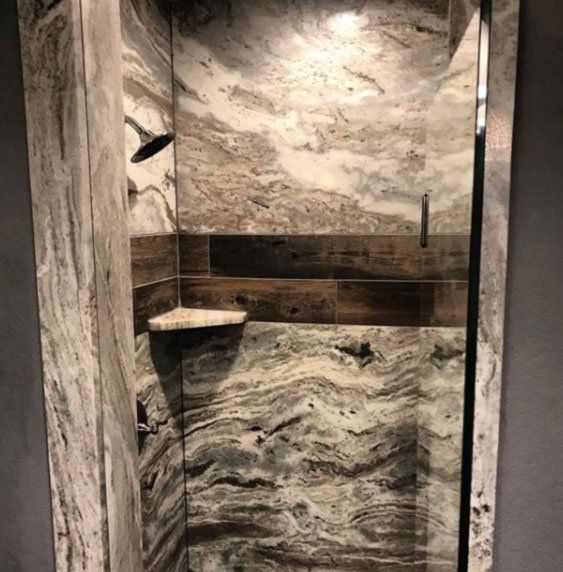 A shower with a marble wall and a glass door.