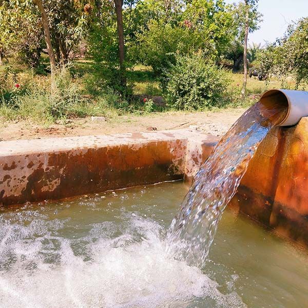 Water pouring from a rusty pipe into a concrete basin in a sunny outdoor setting