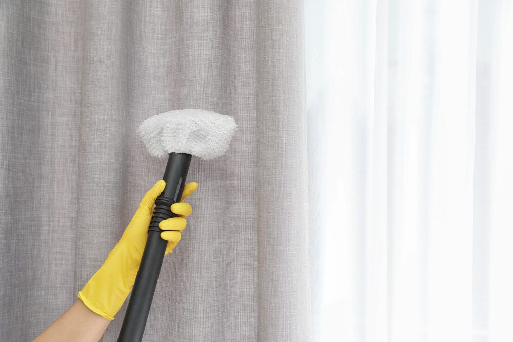 A Person Wearing Yellow Gloves Is Cleaning Curtains with A Duster — Carpet 2 Couch In Condon, QLD