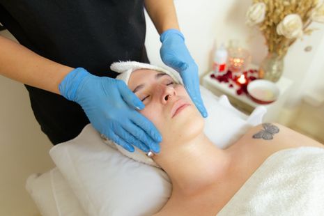 Persona recibiendo un tratamiento facial con una diadema blanca y la mano enguantada de azul; el texto dice “MUCHOS TRATAMIENTOS”.