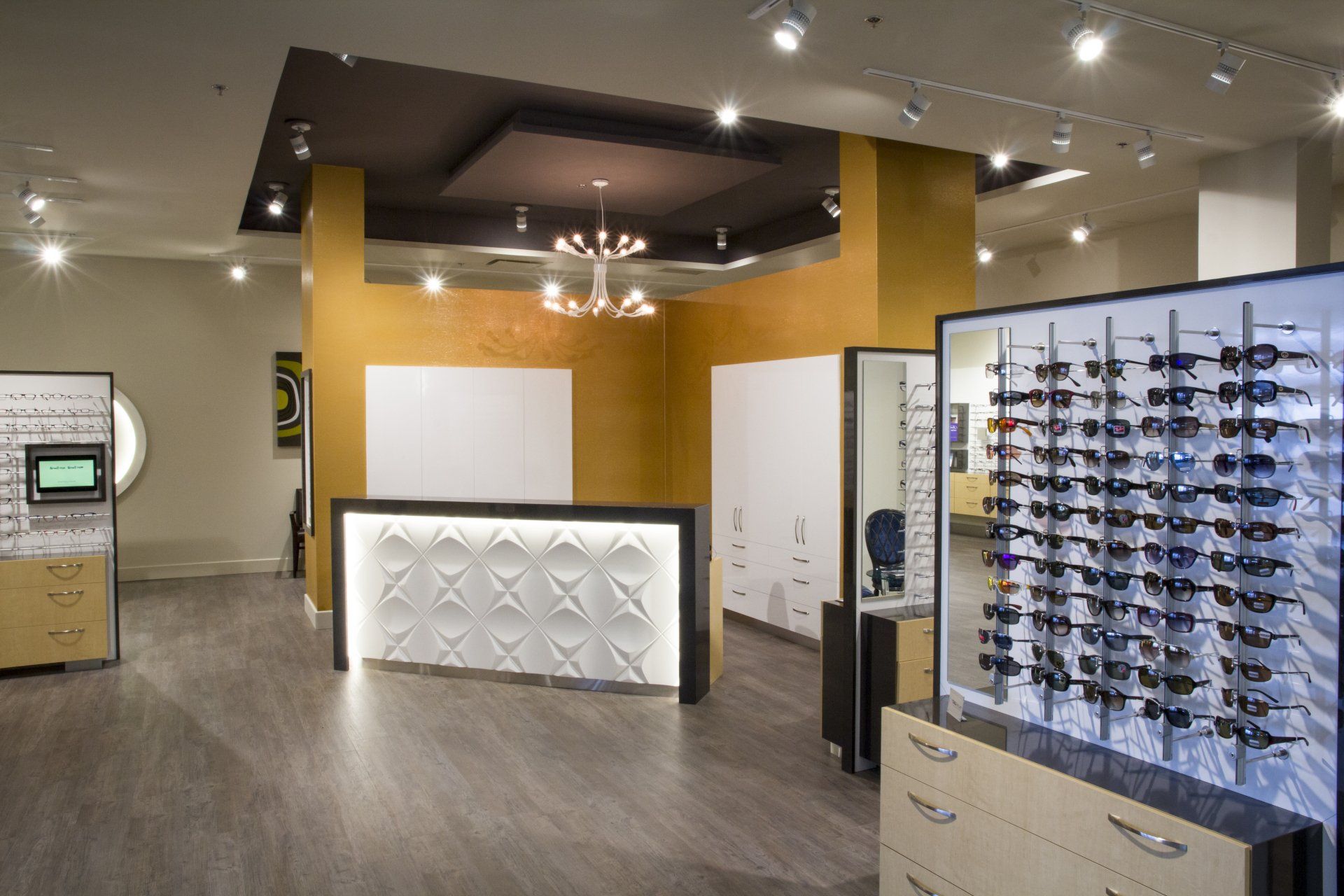 Intérieur d'un magasin d'optométrie avec des présentoirs à lunettes, un comptoir d'accueil et un mur d'accent doré.