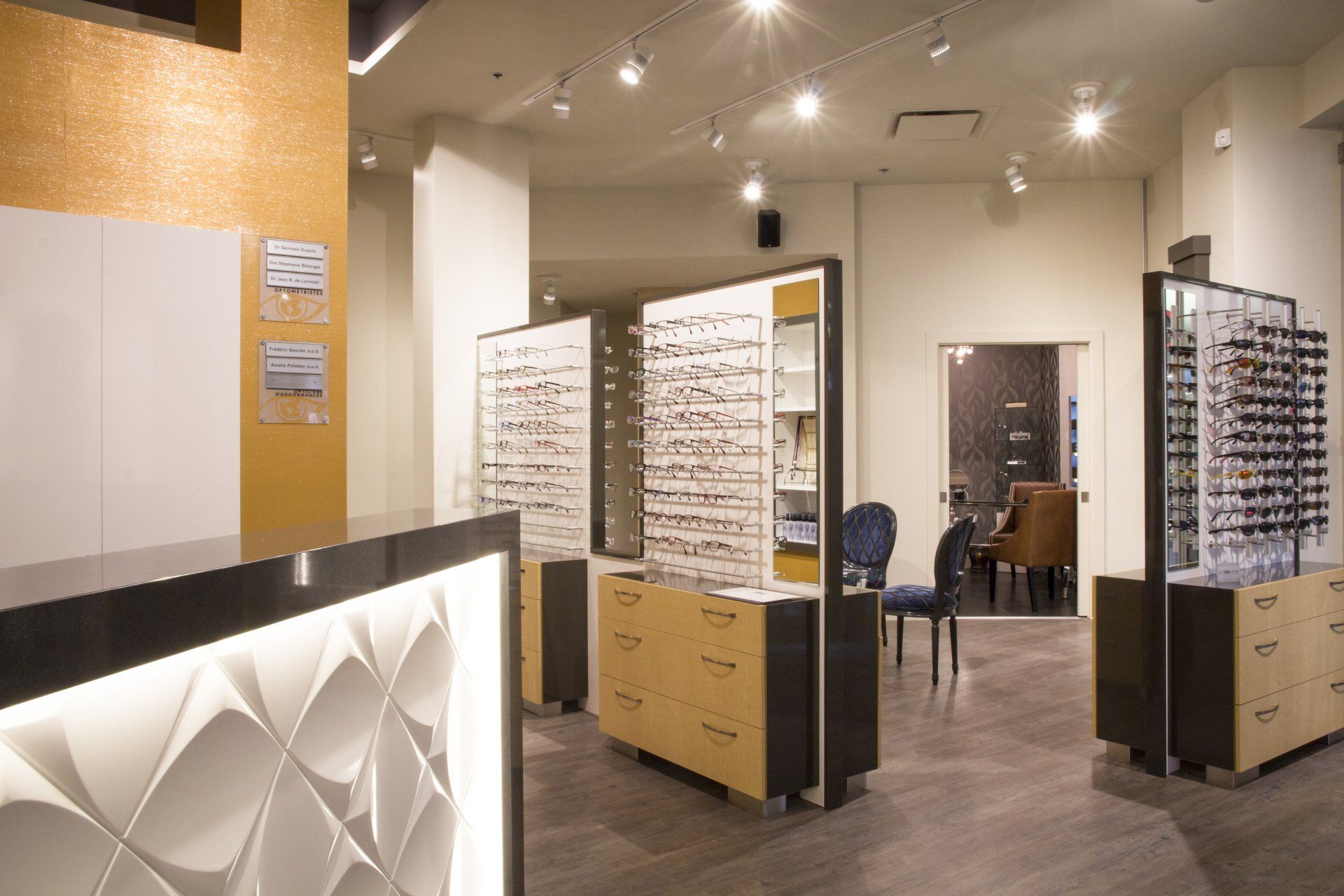 Intérieur d'un magasin d'optique, présentation de lunettes sur présentoirs, design moderne, mur d'accent doré, éclairage vif.