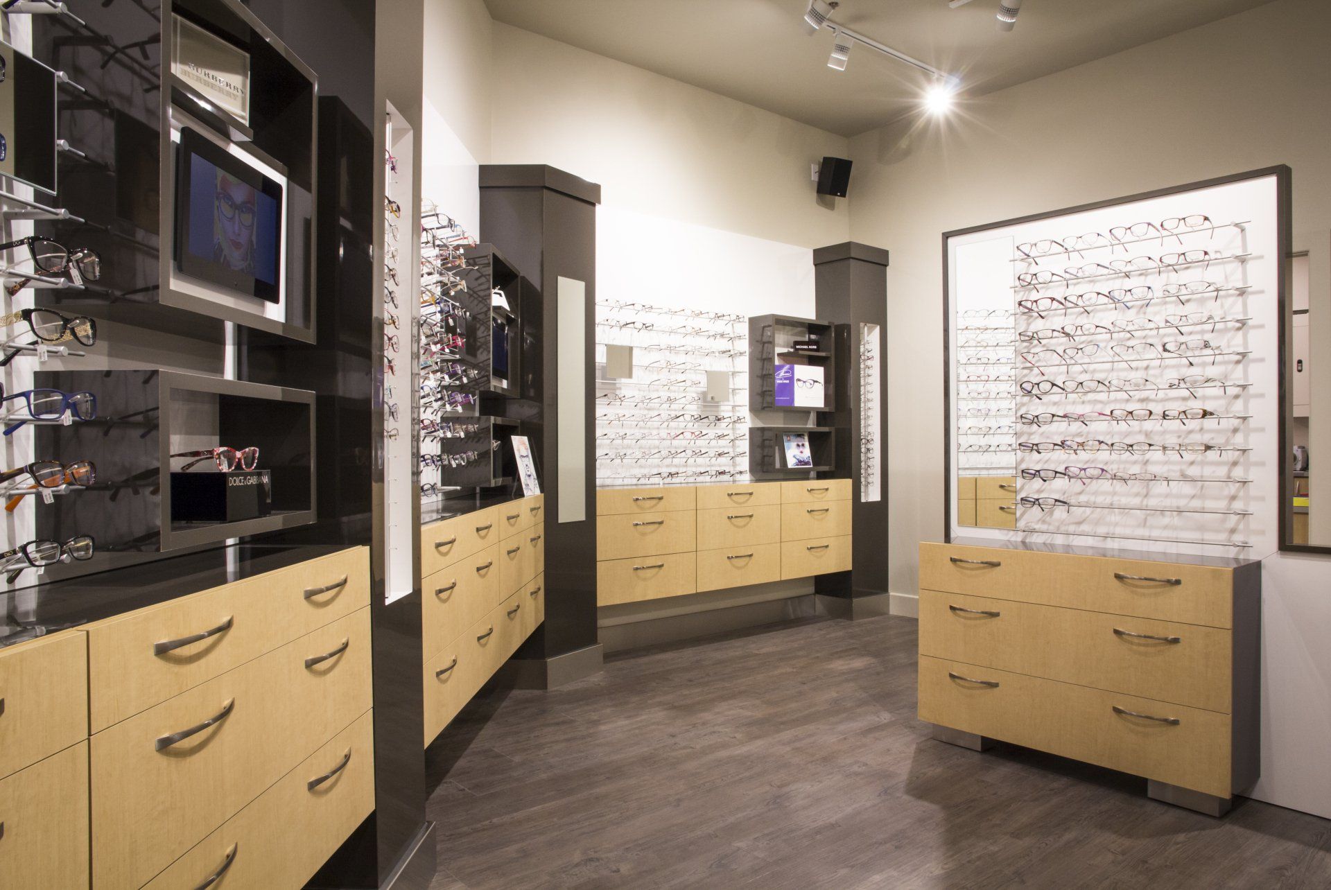 Intérieur d'un cabinet d'opticien. Armoires et montures de lunettes beiges. Sol gris.