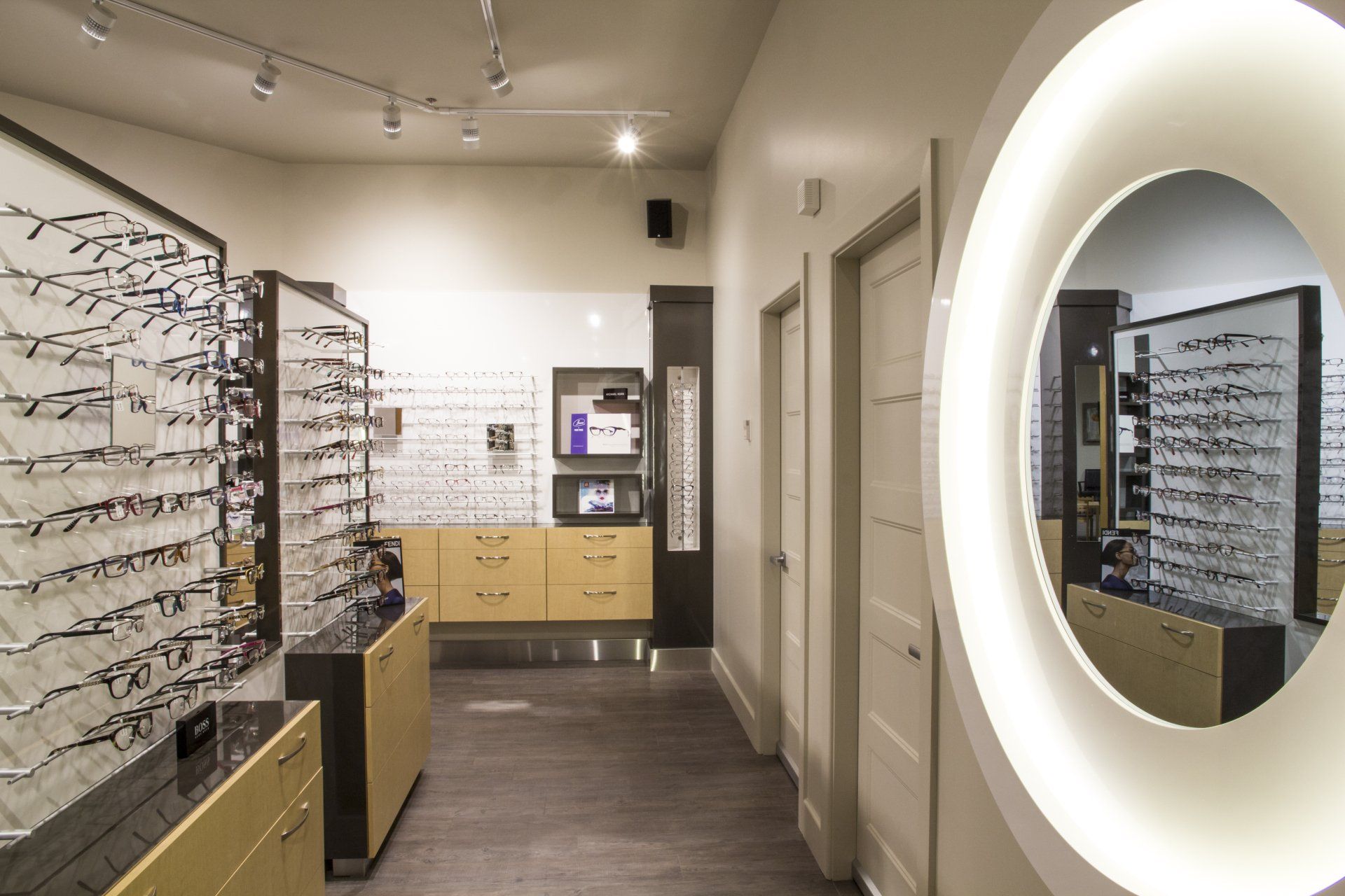 Intérieur d'un magasin d'optique : rangées de montures exposées, miroir ovale, éclairage chaleureux.