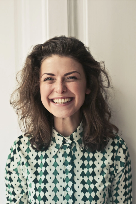 Smiling person with curly hair in a patterned shirt against a light background