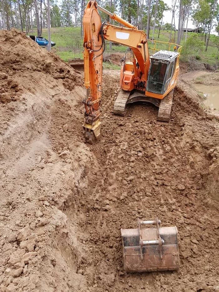 A Large Orange Excavator is Digging a Hole in the Dirt — B E Laser Levelling QLD in Bucca, QLD