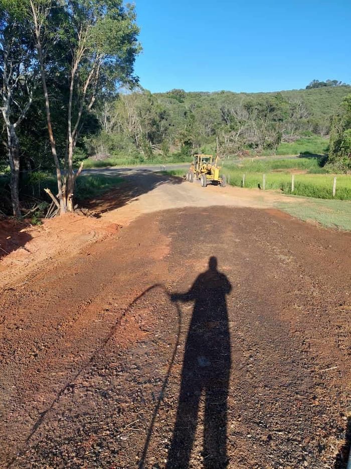 A Shadow of a Person Standing on a Dirt Road With a Bulldozer in the Background — B E Laser Levelling QLD in Bucca, QLD