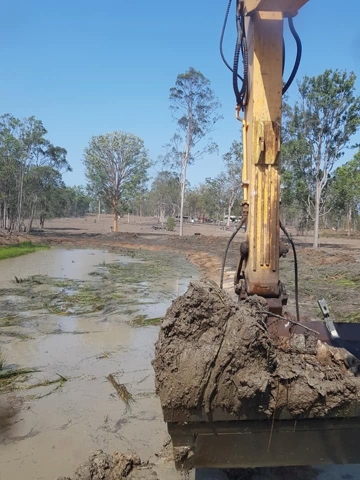 A Yellow Excavator is Digging a Hole in the Mud — B E Laser Levelling QLD in Bucca, QLD